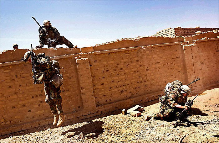 Three US soldiers climbing over a wall