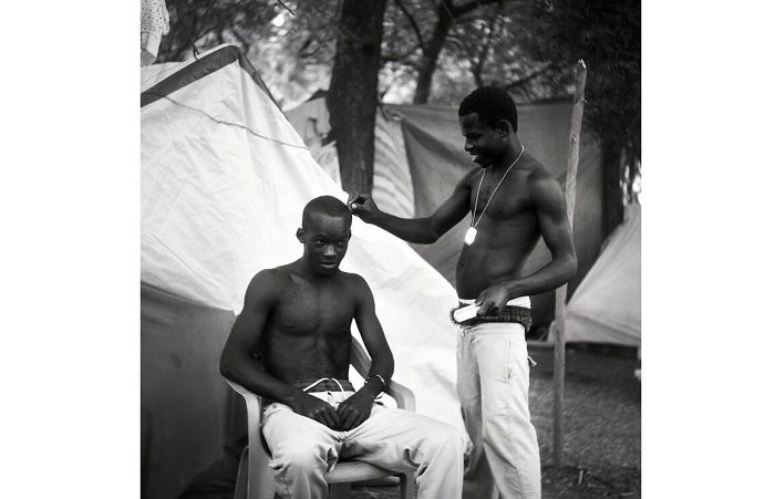 Man cutting another mans hair outside a tent