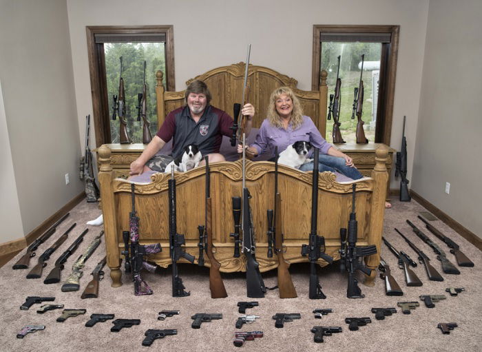 Middle-aged couple sitting on bed surrounded by guns