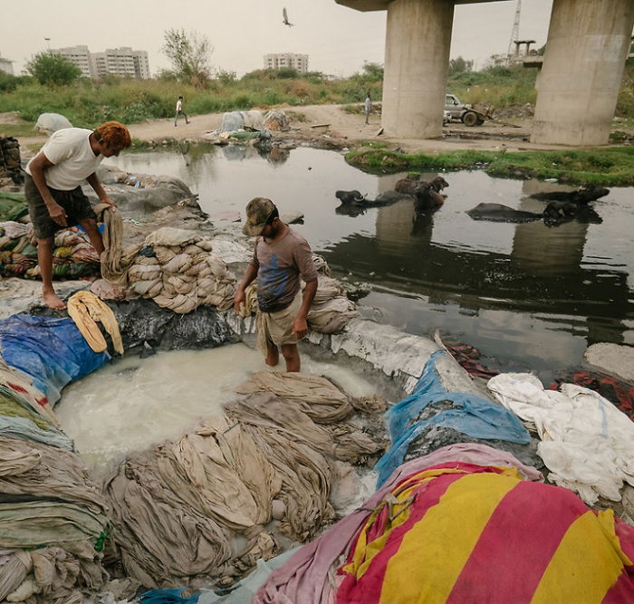 Two men washing clothes under a bridge