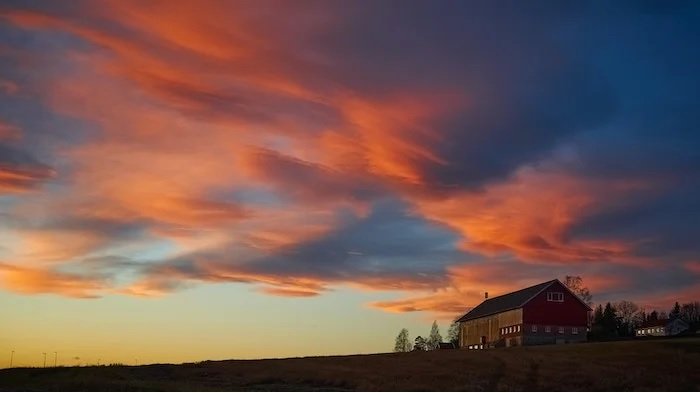 Image of wooden house on a hill at dusk with sun-lit clouds above