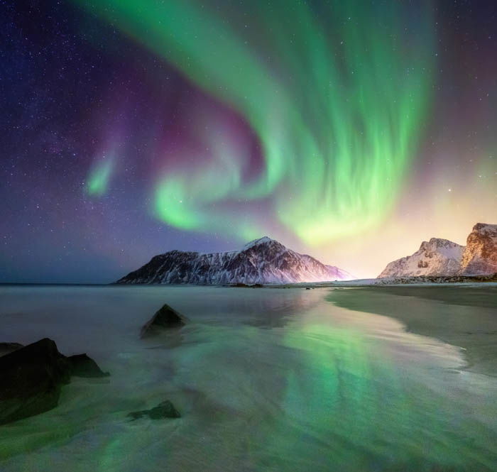 Aurora borealis on the Lofoten islands, Norway. Green northern lights above mountains and beach. Night sky with polar lights. Night winter landscape with aurora. Natural background in the Norway